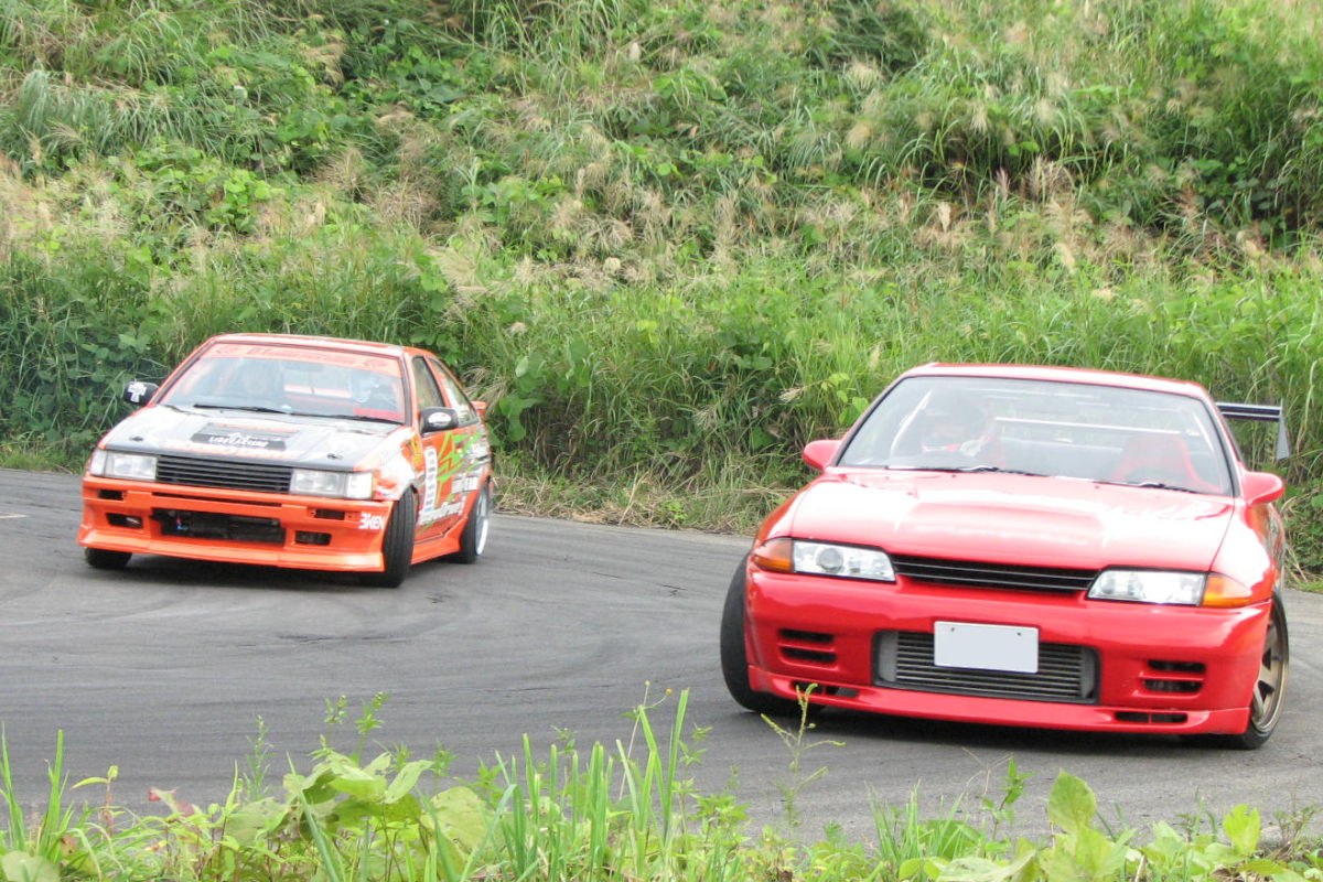 An orange Levin-bodied AE86 running tandem with a red R32 Skyline at a Japanese circuit