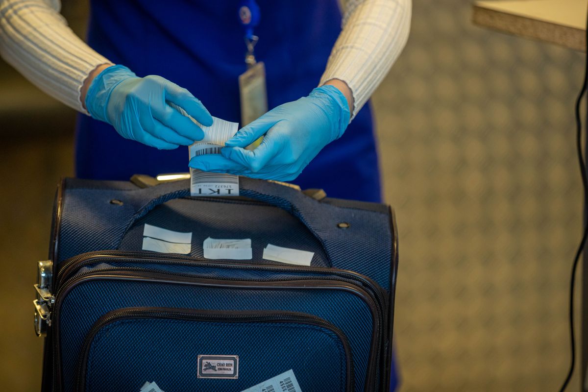 A gloved airport staff member attaching a barcoded tag to a checked suitcase at a counter