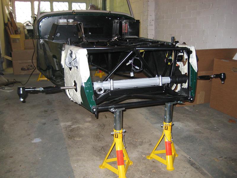 A bare steering rack with rubber boots, inner track rods and track rod ends bolted across the front of a car chassis on axle stands (the car is a Caterham kit car, not a Silvia, Chaser or 350Z)