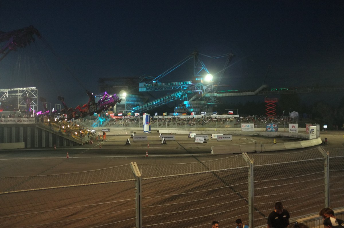 A floodlit drift course laid out between the giant mining machines of Ferropolis, Germany, with a packed grandstand behind