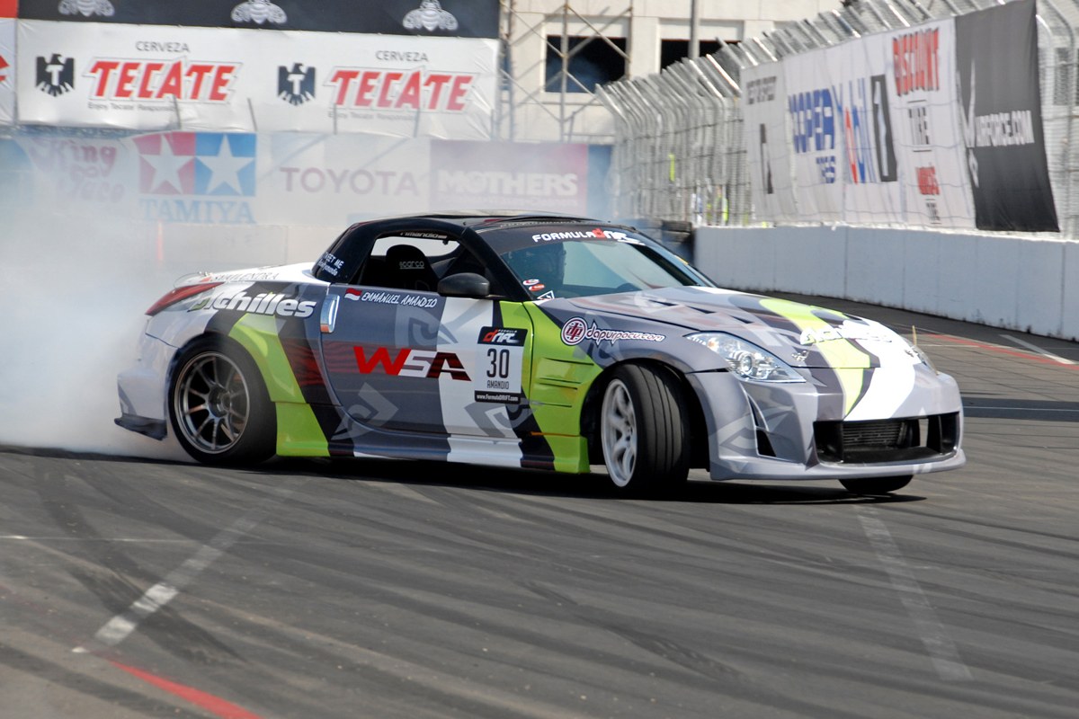 A Formula Drift-liveried Nissan 350Z mid-drift against the concrete walls of a street course