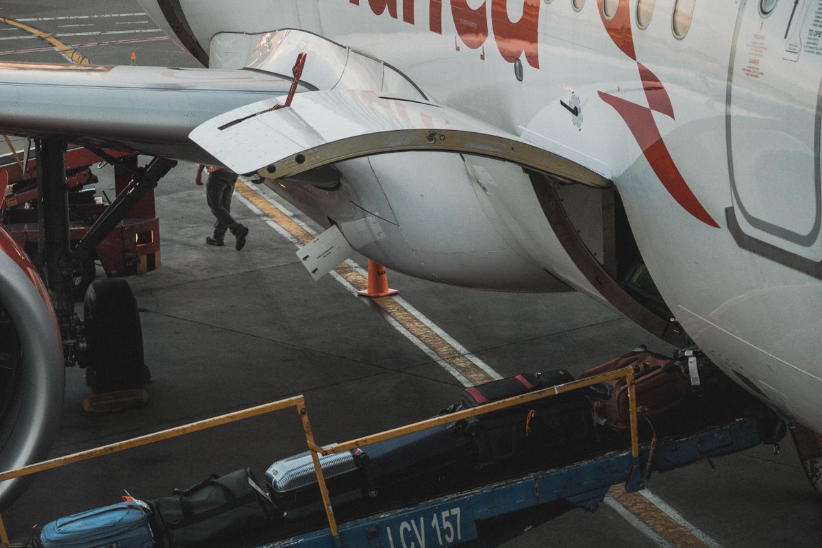 Checked suitcases and soft bags on a belt loader going into the hold of an airliner on the apron