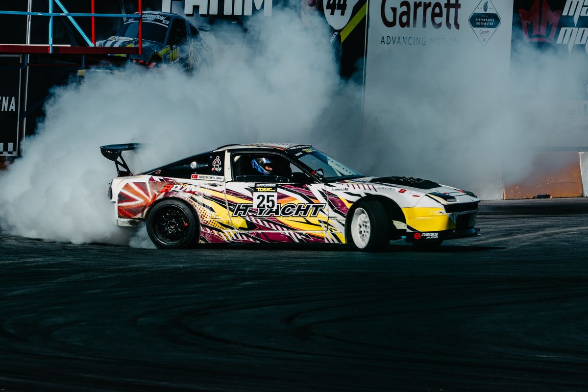 A drift car mid-slide throwing tyre smoke past the kerbs of a Japanese circuit