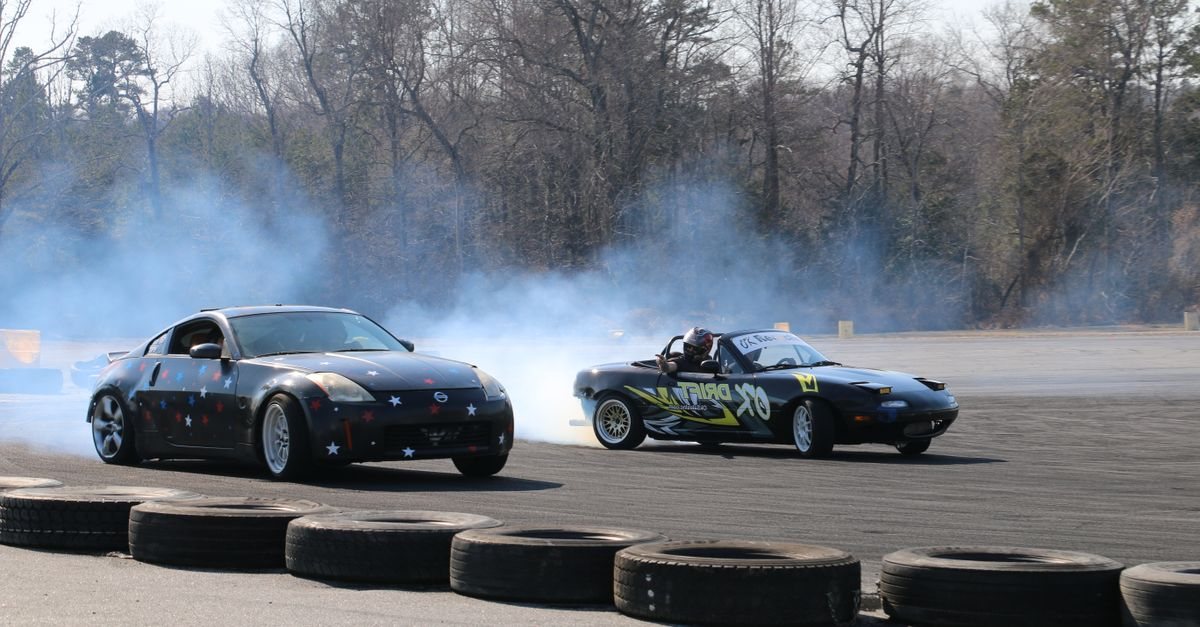 A first-generation Mazda MX-5 drifting beside a Nissan 350Z on a tyre-lined tarmac pad (stock photo, not taken in Japan)