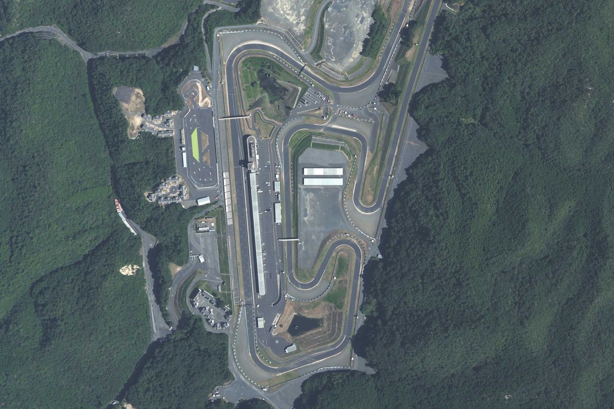 Aerial view of Okayama International Circuit, the pit straight, paddock and grandstands surrounded by forested hills in Mimasaka