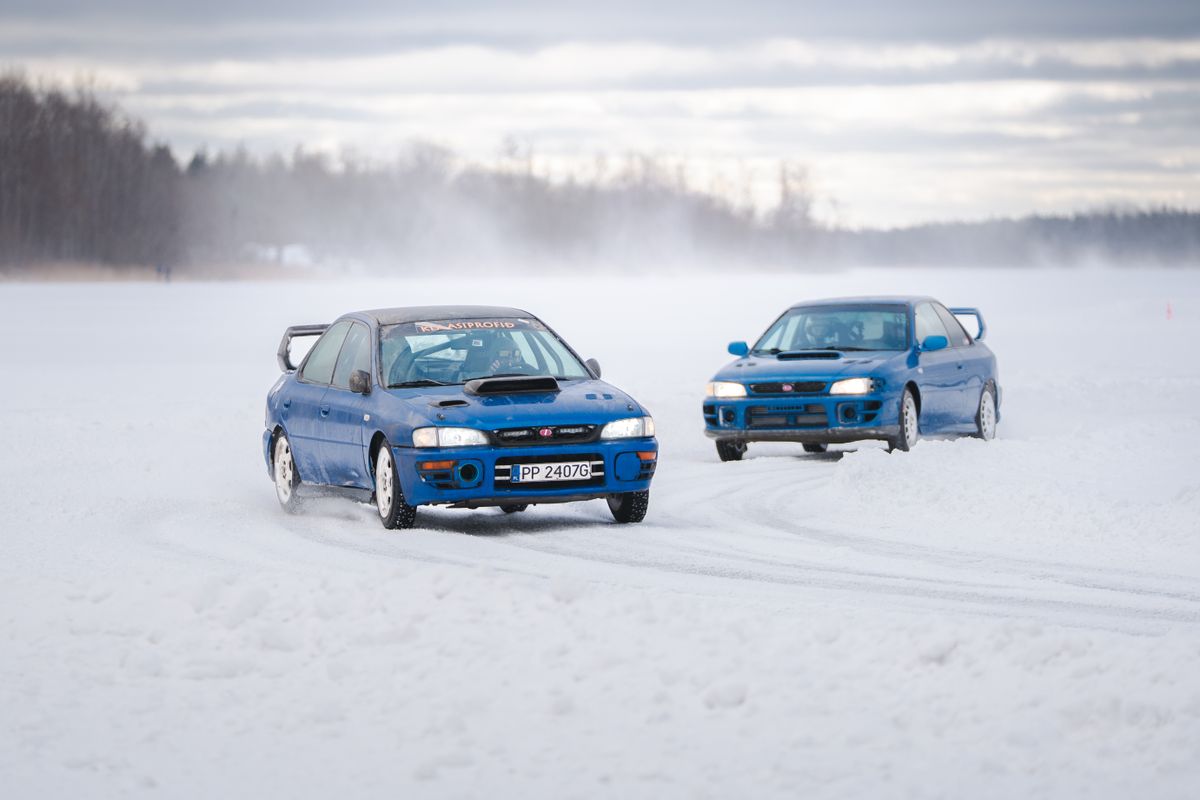 Two blue Subaru Imprezas sliding on a snow-covered course marked out with cones