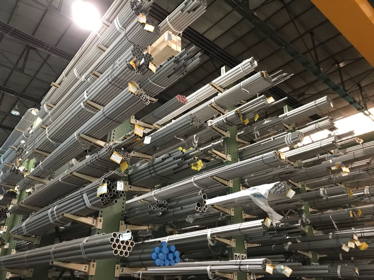 Bundles of long steel tubes stacked on cantilever racking in a warehouse, tagged and strapped