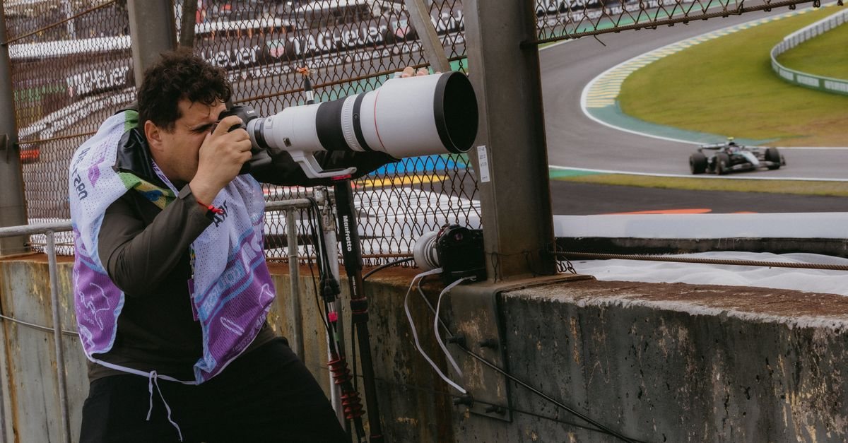 A photographer with a long telephoto lens shooting through a catch fence as a race car passes (stock photo from a Formula 1 race in Brazil, not a Japanese drift event)