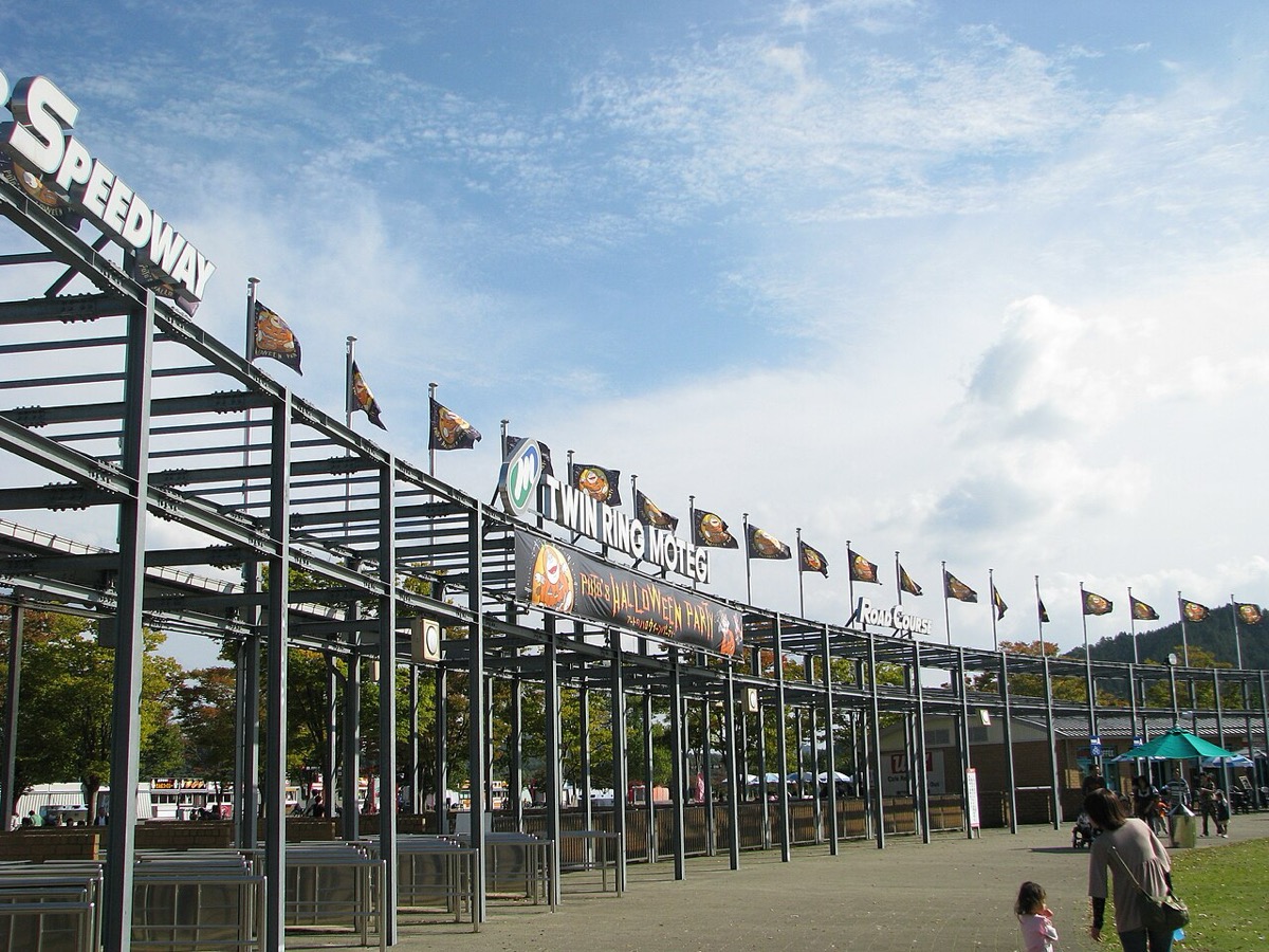 The entrance gate at Motegi in 2008, with the Twin Ring Motegi sign, Road Course and Speedway signs and a row of flags