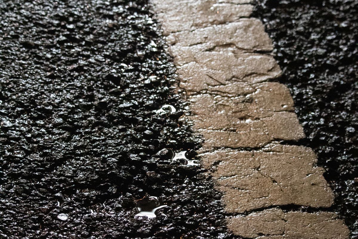 Close-up of soaked asphalt after rain, with water standing along a worn painted line.